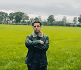 a man with his arms crossed stands in a grassy field