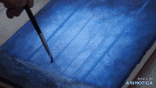 a brush is being used on a piece of blue paper that says made in animatica