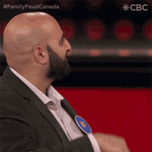 a bald man with a beard is sitting in front of a screen that says ' family feud canada ' on it