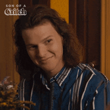 a man with long hair is smiling in front of a sign that says son of a witch