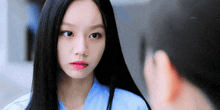 a woman with long black hair wearing a blue shirt looks at the camera