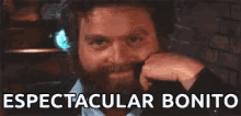 a man with a beard is smiling and looking at the camera with the words spectacular bonito behind him .
