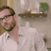 a man with a beard wearing glasses and a white shirt is looking at the camera .