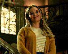 a woman wearing a yellow cardigan and striped shirt is smiling