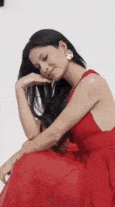 a woman in a red dress is sitting down with her head resting on her hands .