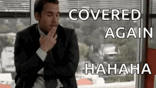 a man in a suit and tie is sitting in front of a window covering his mouth .