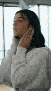 a woman in a white sweatshirt adjusts her hair