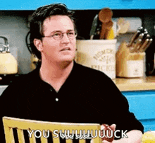 a man is sitting in a chair in a kitchen holding an apple and saying `` you suck '' .