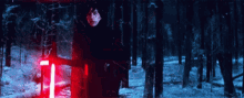 kylo ren is holding a red lightsaber in the woods .