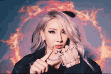 a woman with a lot of rings on her fingers is standing in front of a fire background