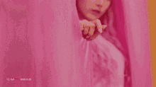 a woman with pink hair is standing in front of a pink and orange curtain .