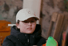 a young girl wearing a white hat and glasses is holding a green object .