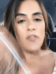 a woman wearing hoop earrings is sitting in a car and looking at the camera .