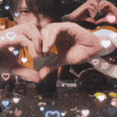 a person making a heart with their hands with hearts around them