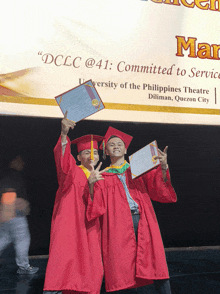 two graduates holding up their diplomas in front of a sign that says " dcclc @ 41 "
