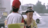 a man in a hat is talking to another man in a parking lot while another man says `` have a seat '' .
