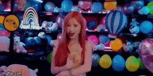 a woman with red hair is holding a teddy bear in front of balloons and stuffed animals