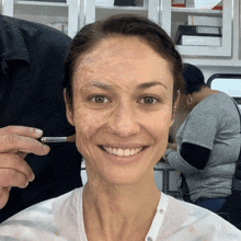 a woman is smiling while getting her face painted with a brush