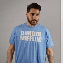 a man wearing a blue shirt that says dunder mifflin paper company is asking what