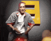 a man in a grey jacket is standing in front of a yellow letter e
