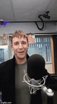 a man is smiling in front of a microphone in a room with pictures on the wall behind him