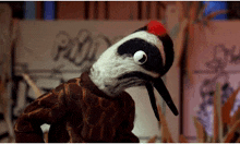 a stuffed bird with a red beak is standing in front of a sign that says ' plain '