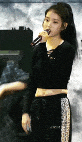 a woman is singing into a microphone while wearing a black crop top and leopard print pants