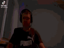 a man wearing headphones and a puma shirt is dancing in a room .