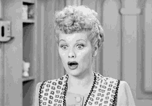 a black and white photo of a woman with curly hair making a surprised face .