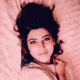 a woman is laying on a bed with her head on a pillow and looking at the camera .