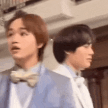 two men in suits and bow ties are standing next to each other and looking at something .