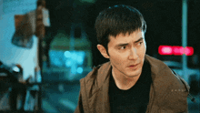 a man in a brown jacket stands in front of a red sign that says o