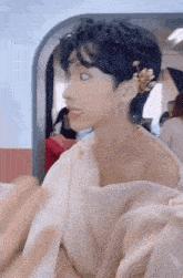 a young man wearing a white dress and a gold necklace is looking at the camera .