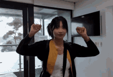 a woman flexes her muscles in front of a large window