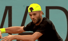 a man wearing a black shirt and a yellow hat playing tennis