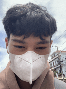a man wearing a white face mask looks at the camera with a building in the background