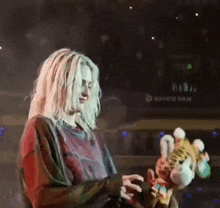 a woman with long blonde hair is holding a stuffed animal on a stage .