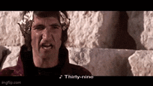 a man with a laurel wreath on his head is standing in front of a stone wall and says thirty-nine .