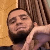 a man with a beard is making a funny face while sitting in front of a window .