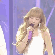 a woman singing into a purple microphone while wearing earrings