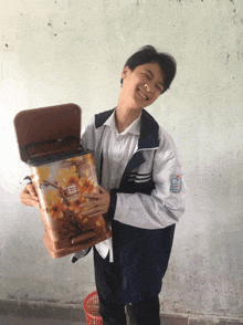 a young man in a white shirt and blue jacket holds a container with a floral design on it