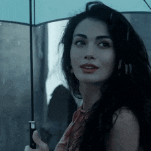 a woman holding an umbrella in the rain looks at the camera
