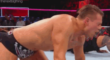 a man is crawling on the ground in a wrestling ring while another man watches .