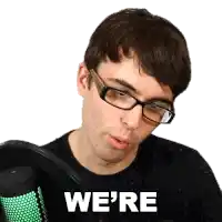 a man wearing glasses is sitting in front of a microphone and says we 're