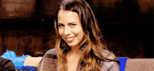 a woman in a plaid shirt is smiling for the camera while sitting on a couch .