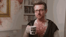 a man with blood on his shirt is holding a mug that says `` don t mug me '' .