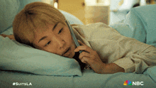 a woman laying on a bed talking on a cell phone with a nbc logo behind her