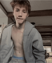 a young man without a shirt is wearing a gray hoodie and blue underwear .