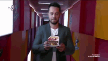 a man in a suit is holding a cake in front of a tv screen