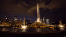 a fountain is lit up at night with a city in the background